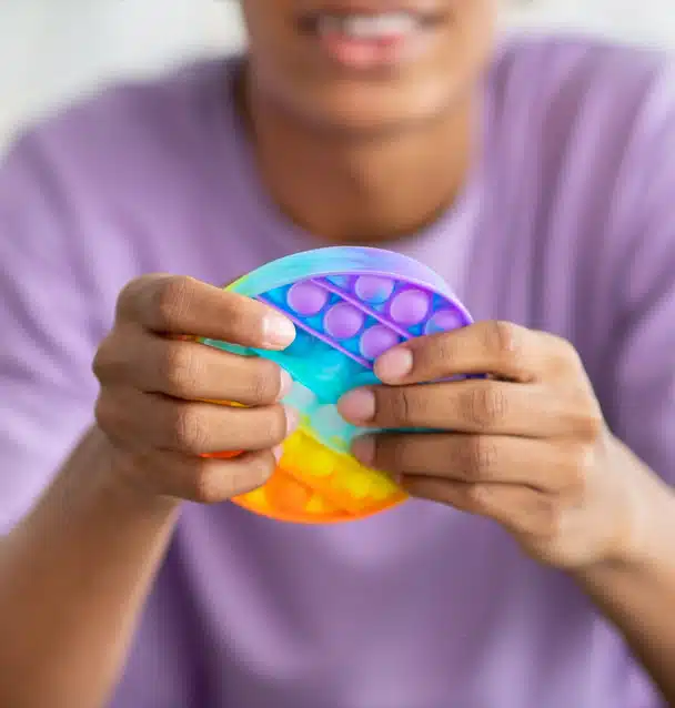 a fidget toy held in the foreground by a blurry young person wearing a purple shirt